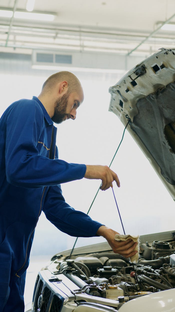 Mechanic inspecting car engine oil with dipstick in an automotive repair shop.